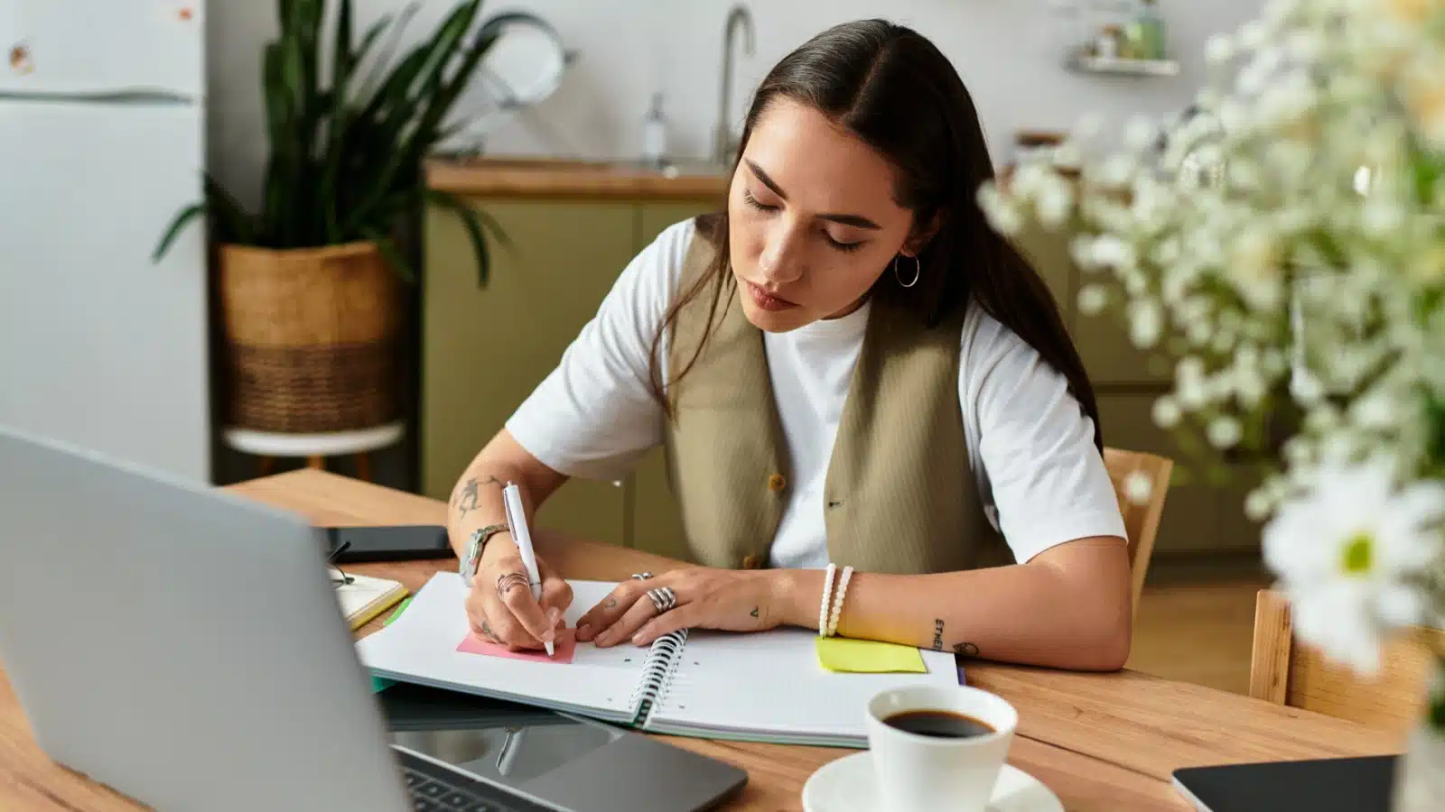 A woman sits at a computer writing notes in her planner.