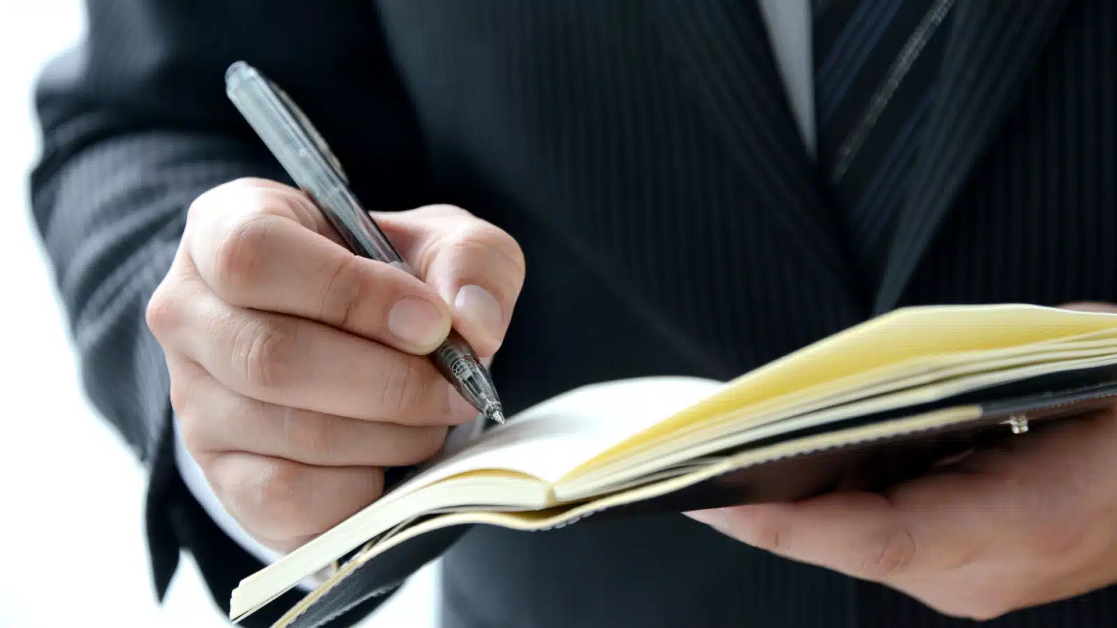 Close up of a business man writing notes in a sleek, professional manner planner.
