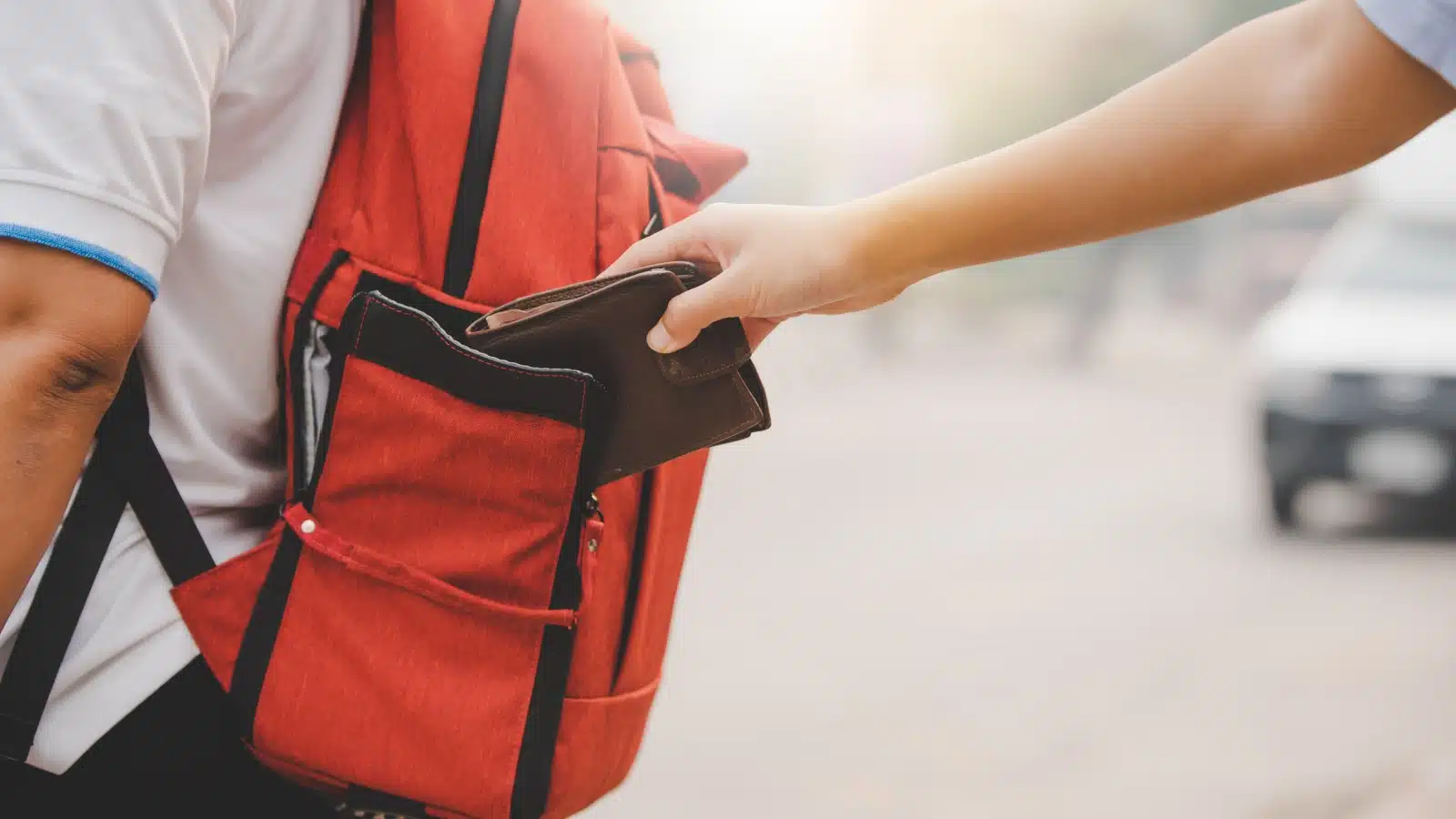 A pickpocket stealing out of a rear-facing backpack.