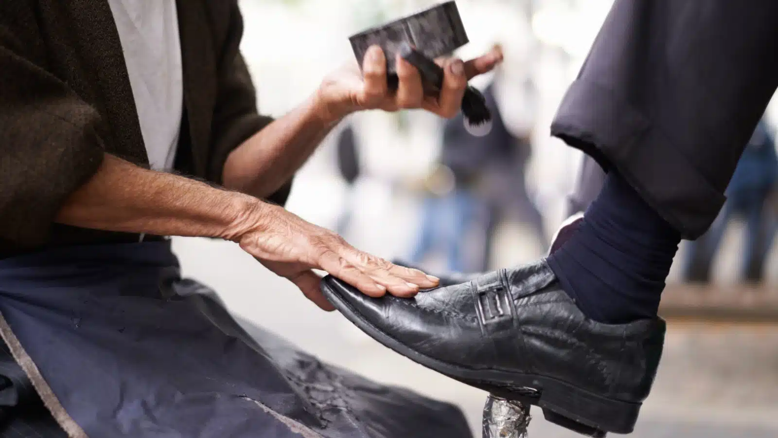 A shoe shiner cleans a businessman's shoes.