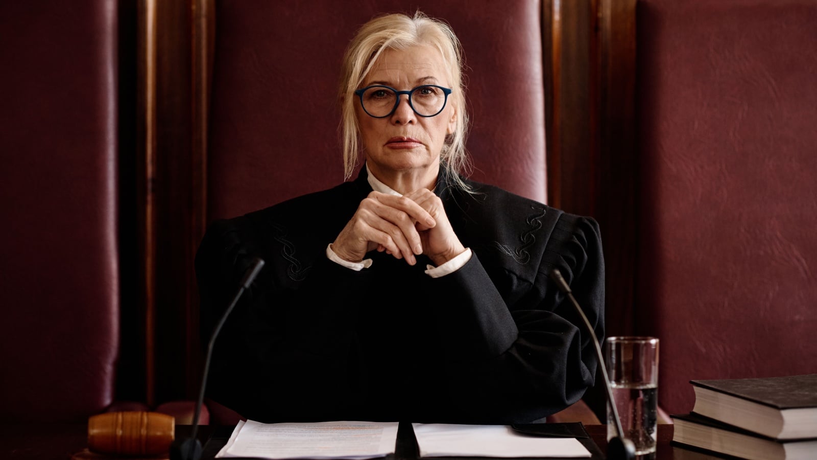 A judge on the bench, stoically watching proceedings with a hardened look on her face. She's judging us all.