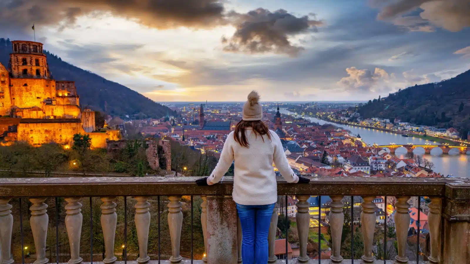A tourist looks out at the city of Heidelberg from near the castle during a winter sunset.
