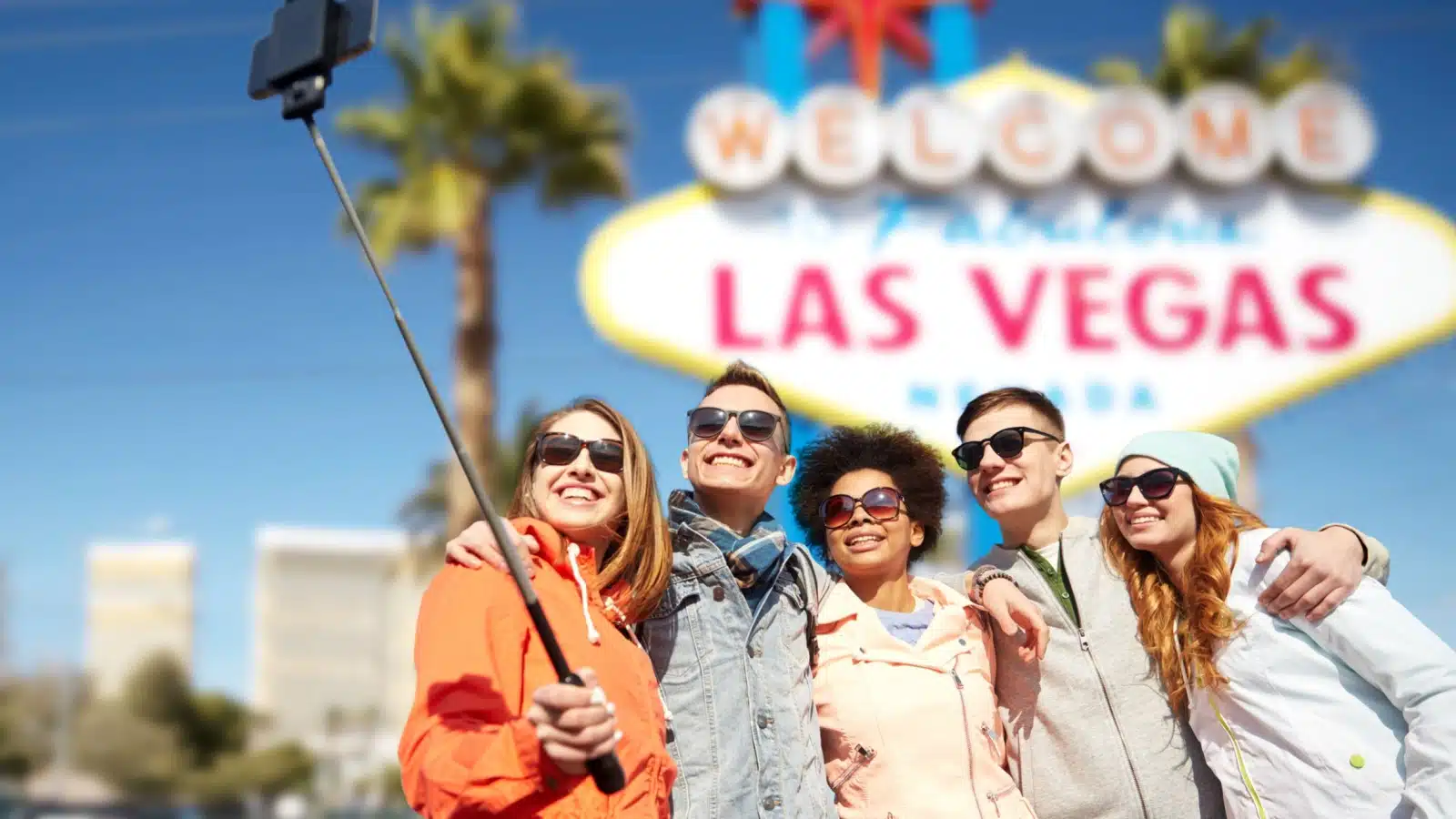 A group of tourists taking a selfie in front of the "Welcome to Las Vegas" sign.
