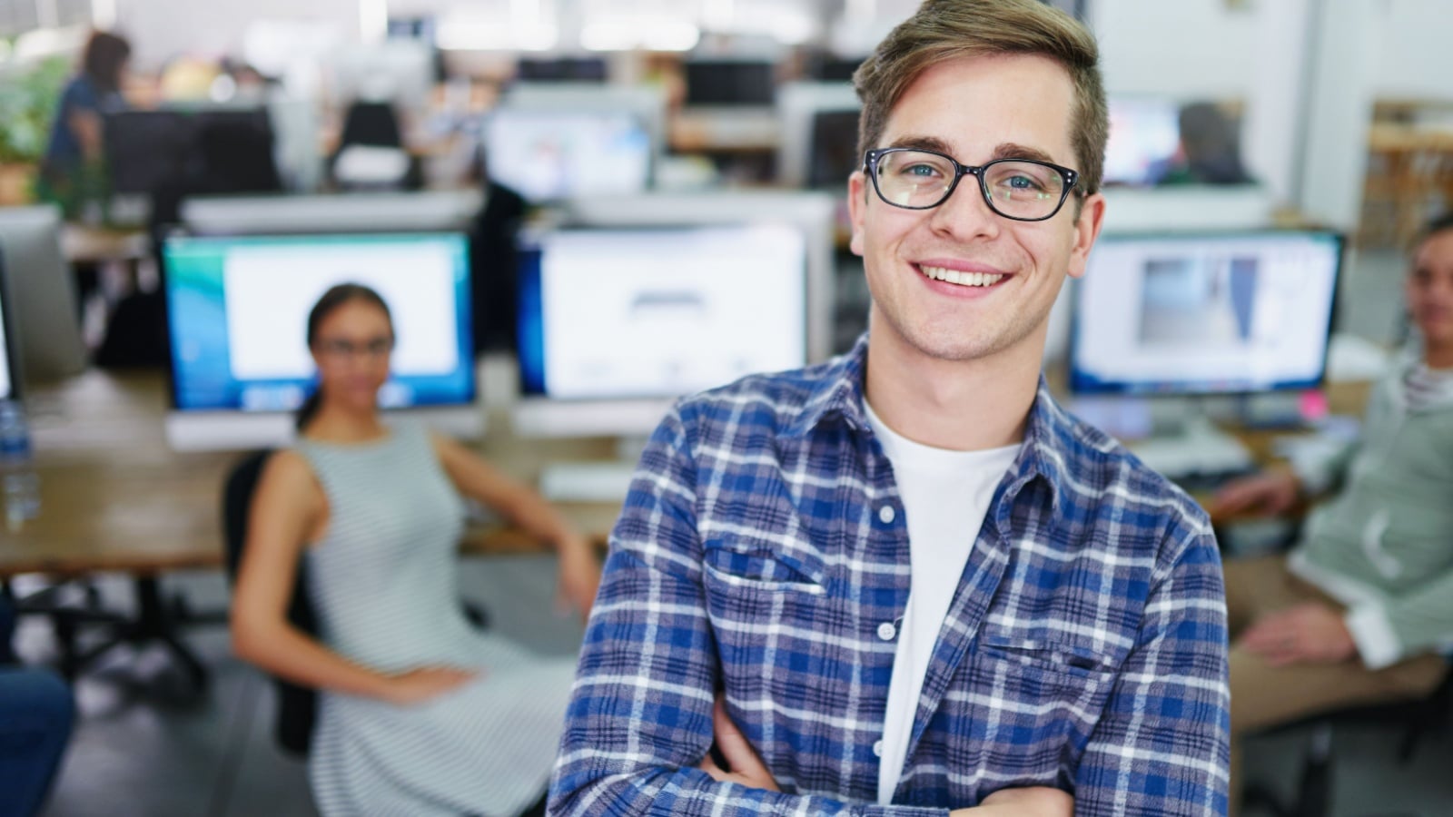 A smiling young man at workplace surrounded by computers to represent unpaid internships.