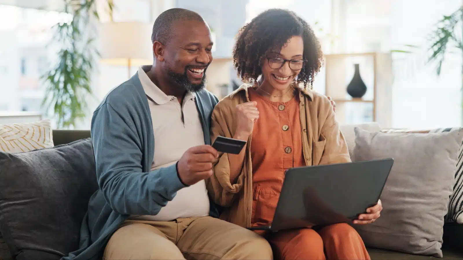 A happy couple sits at a laptop, holding a credit card, to represent how to leverage credit card rewards points.