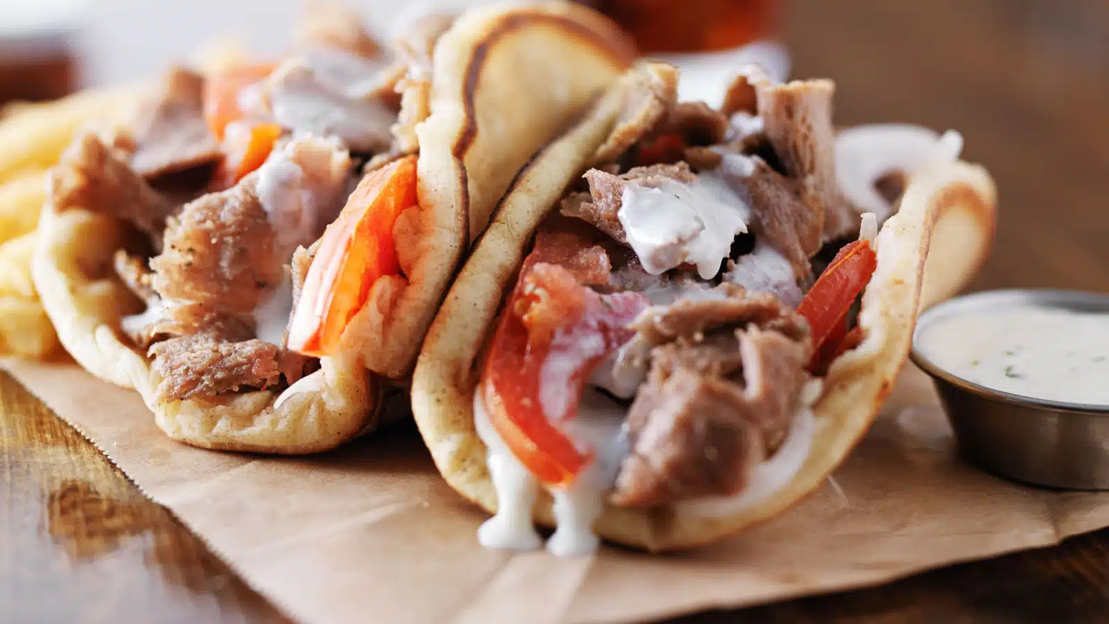 Two gyro sandwiches with perfectly fried pita bread, topped with tzatziki sauce and tomato. Served with fries.
