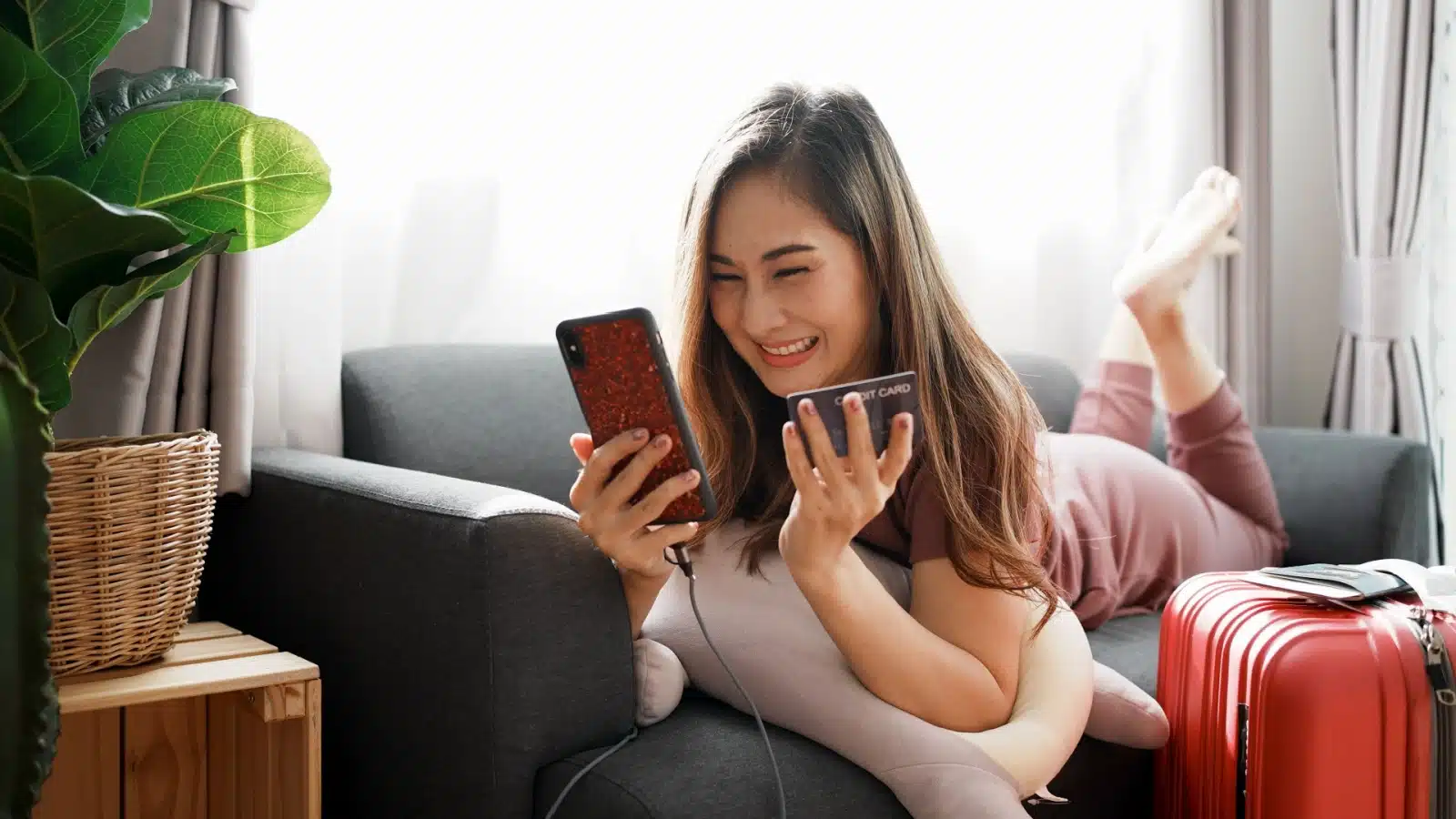 A happy woman uses her phone and credit card for online shopping. 