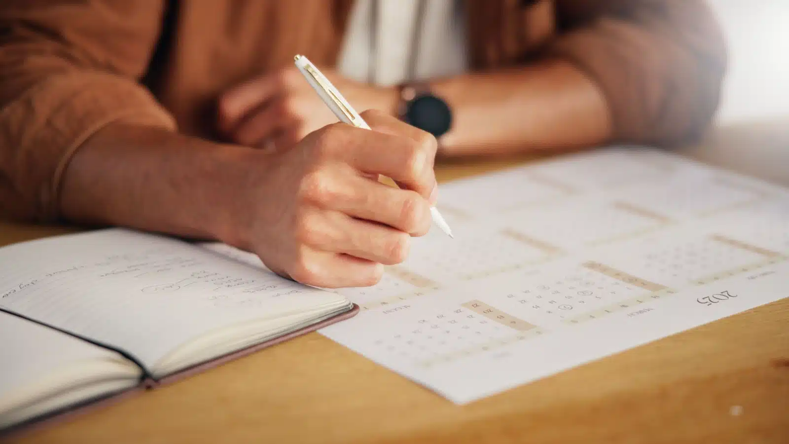 Close up of a person using both a journal and a planner on their desk.