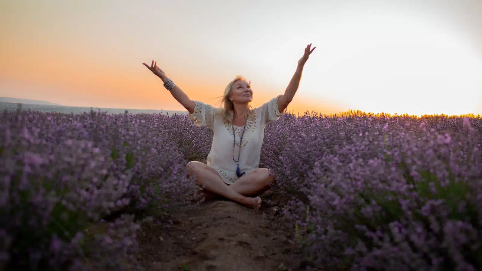 A middle aged woman sitting among flowers celebrating nature's bounty surrounding her.