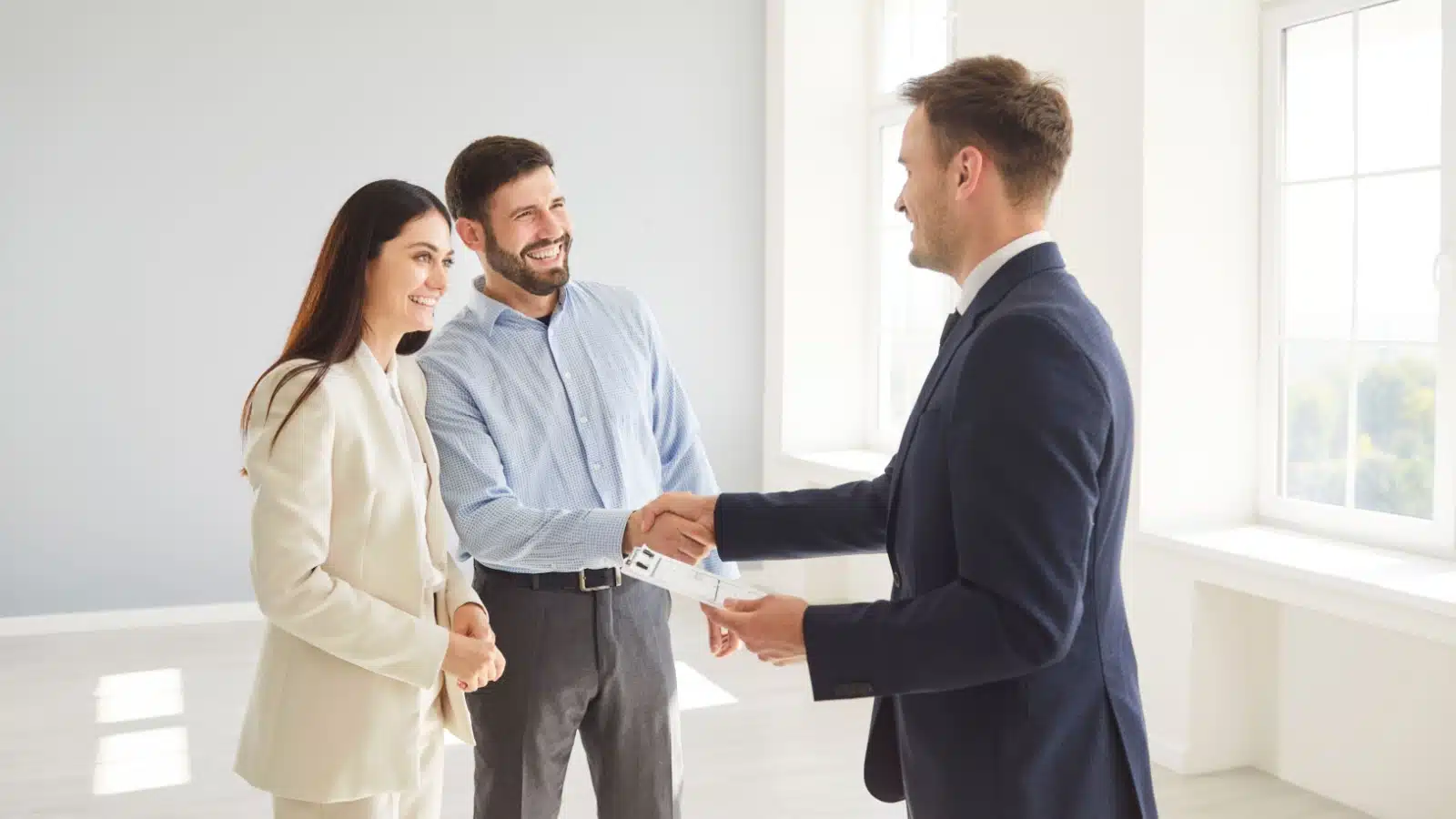 A real estate agent shakes hands with a couple in an empty home. 