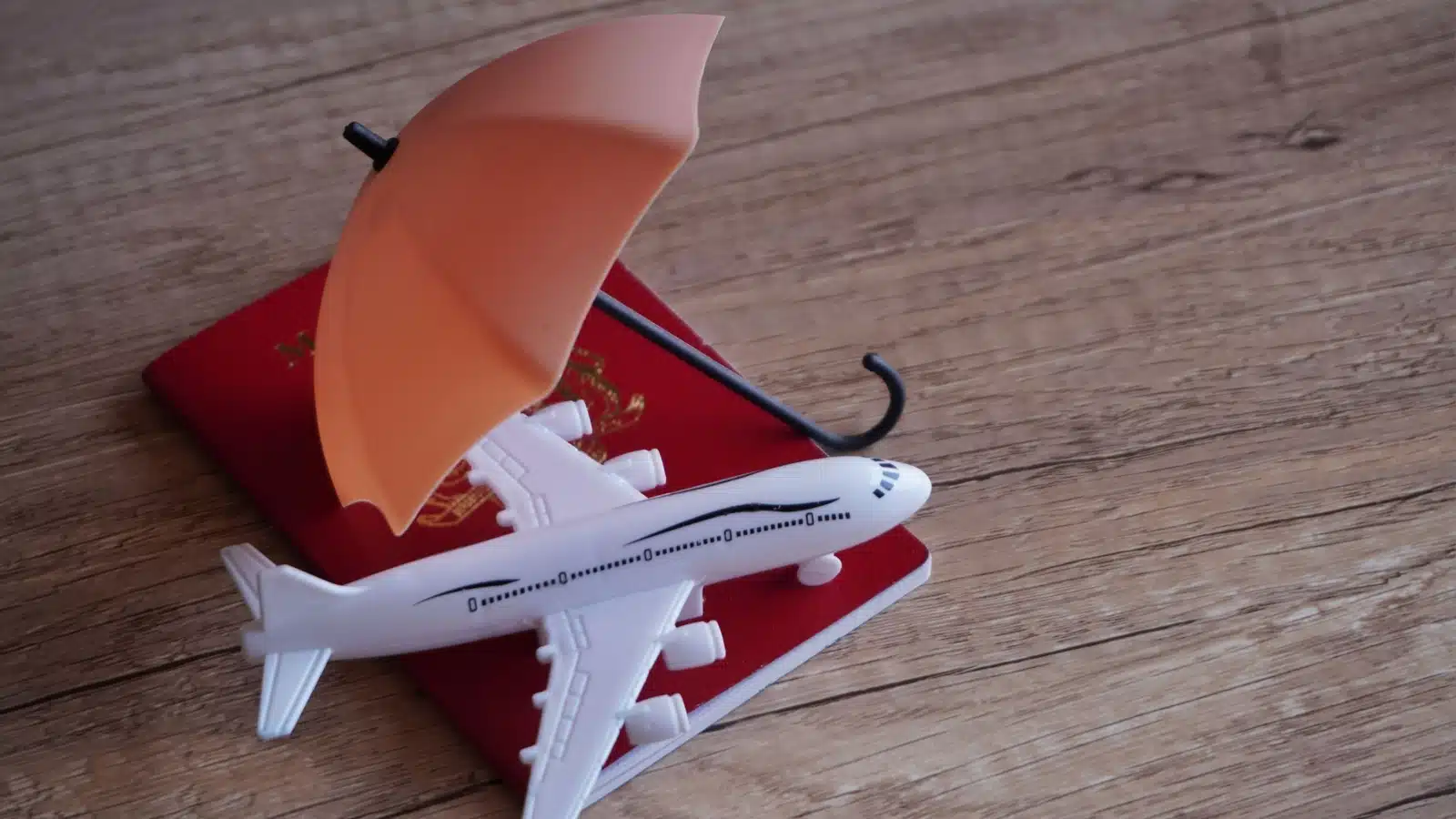 A model plane on top of a passport with an umbrella over them to represent travel insurance.