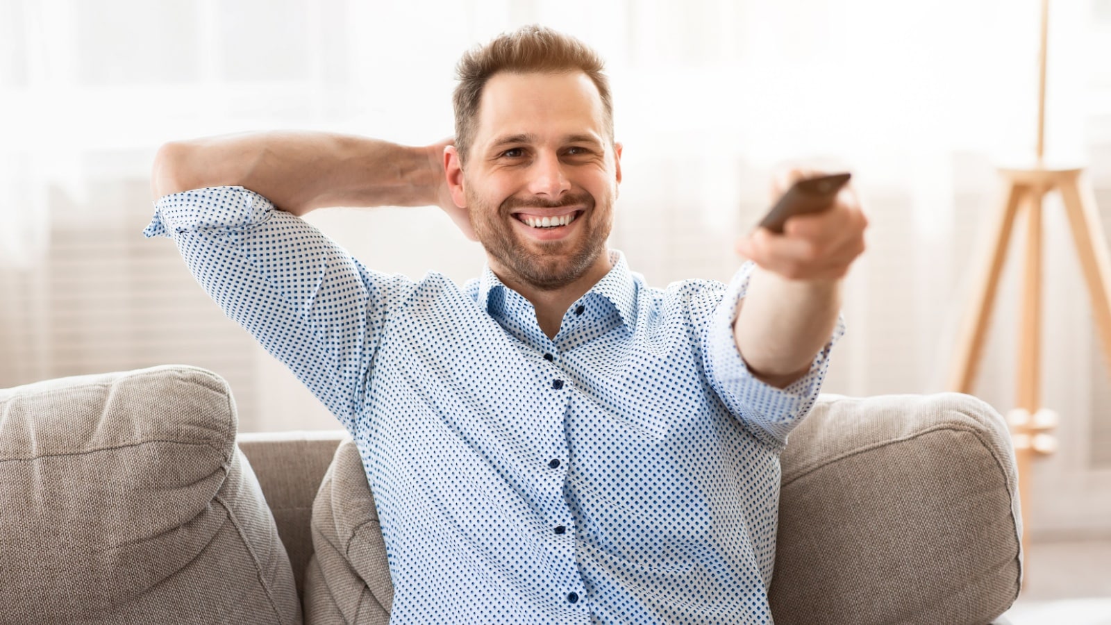 A happy man watching television, pointing his remote control.