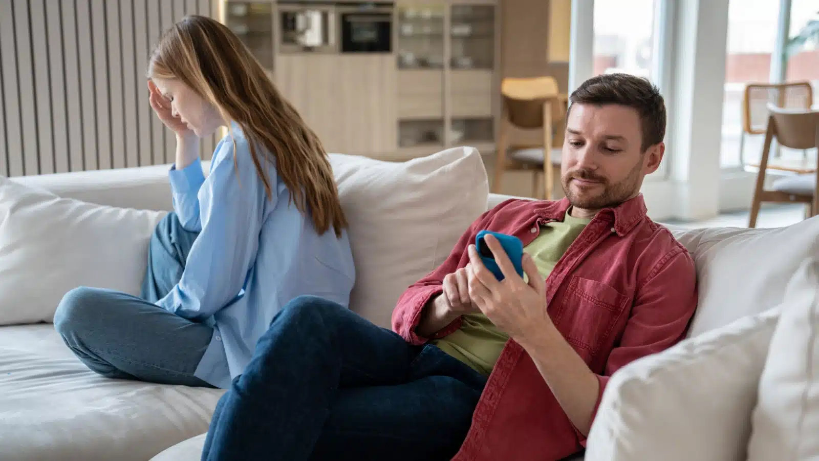 An unbothered man looks at his phone while his girlfriend cries. He doesn't care that she's unhappy.