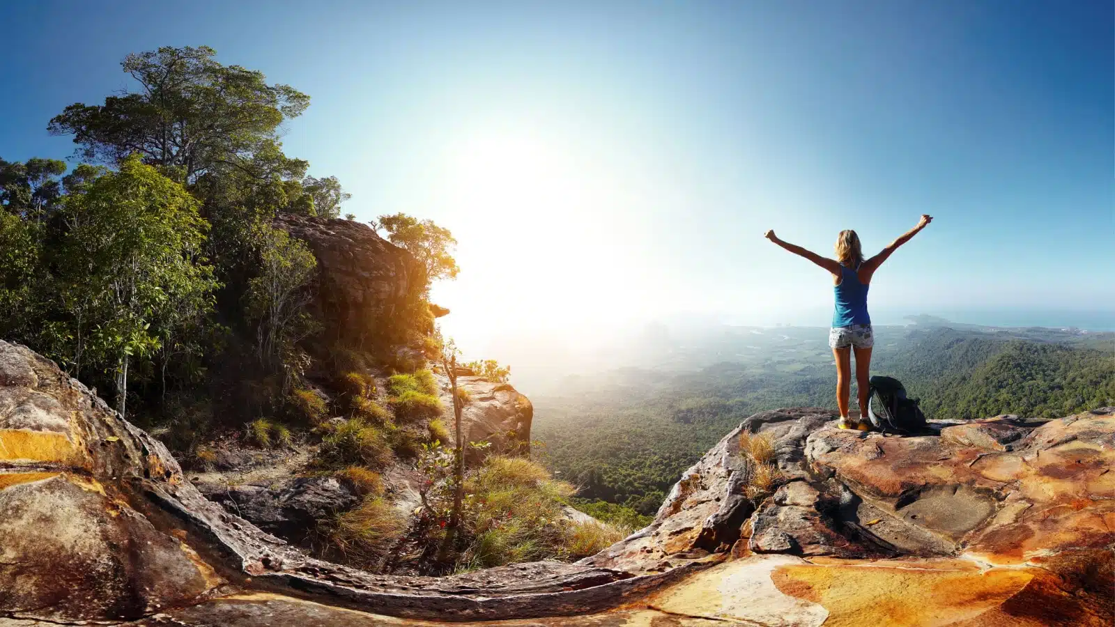A woman standing on a mountain top with her arms up celebrating the long hike.