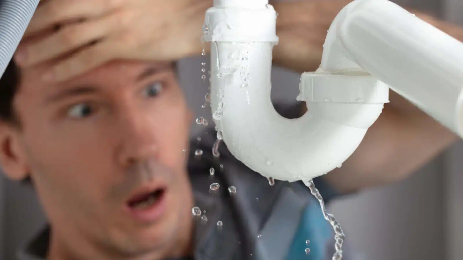 An upset man looking at a leaking pipe in his home.