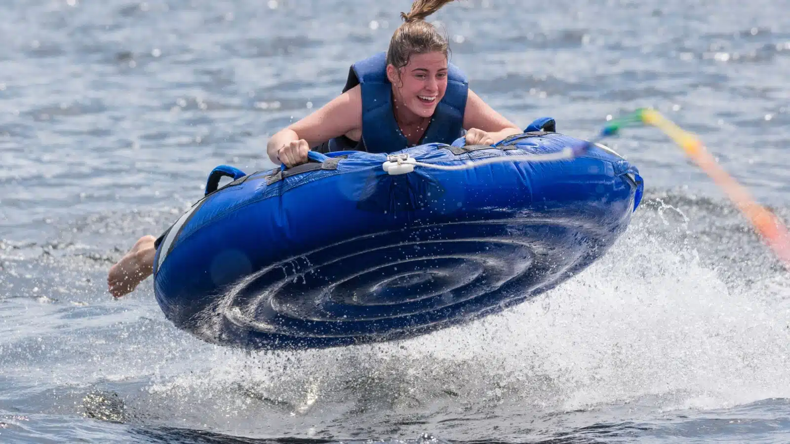 A young girl holding onto an intertube as it's being pulled through the water.