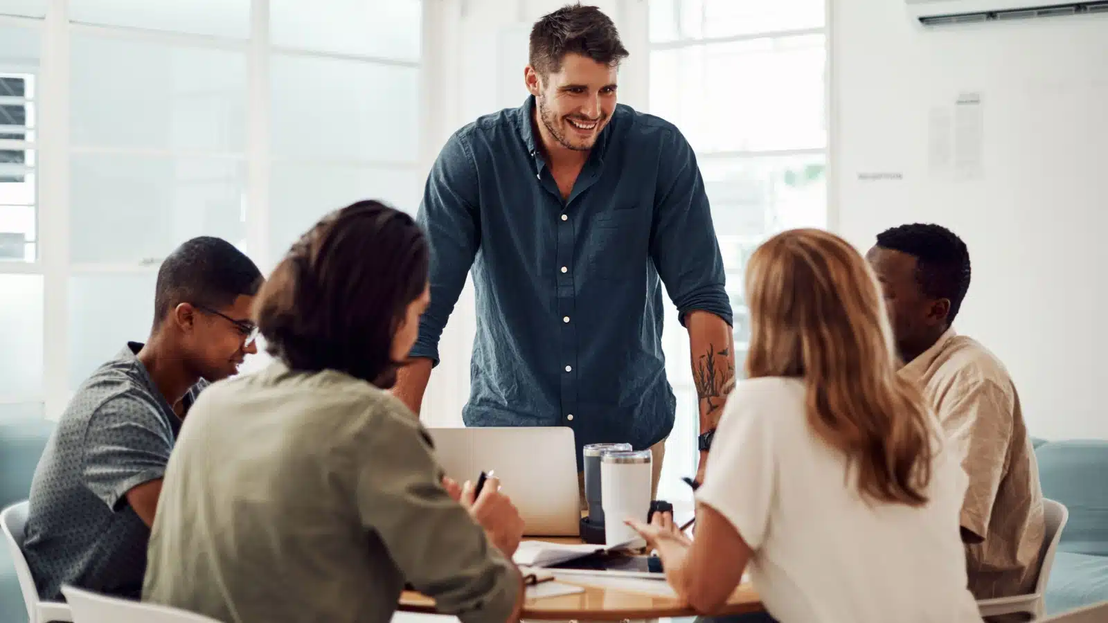 A leader stands in front of the group, smiling. The team is in a circle, representing teamwork and collaboration.