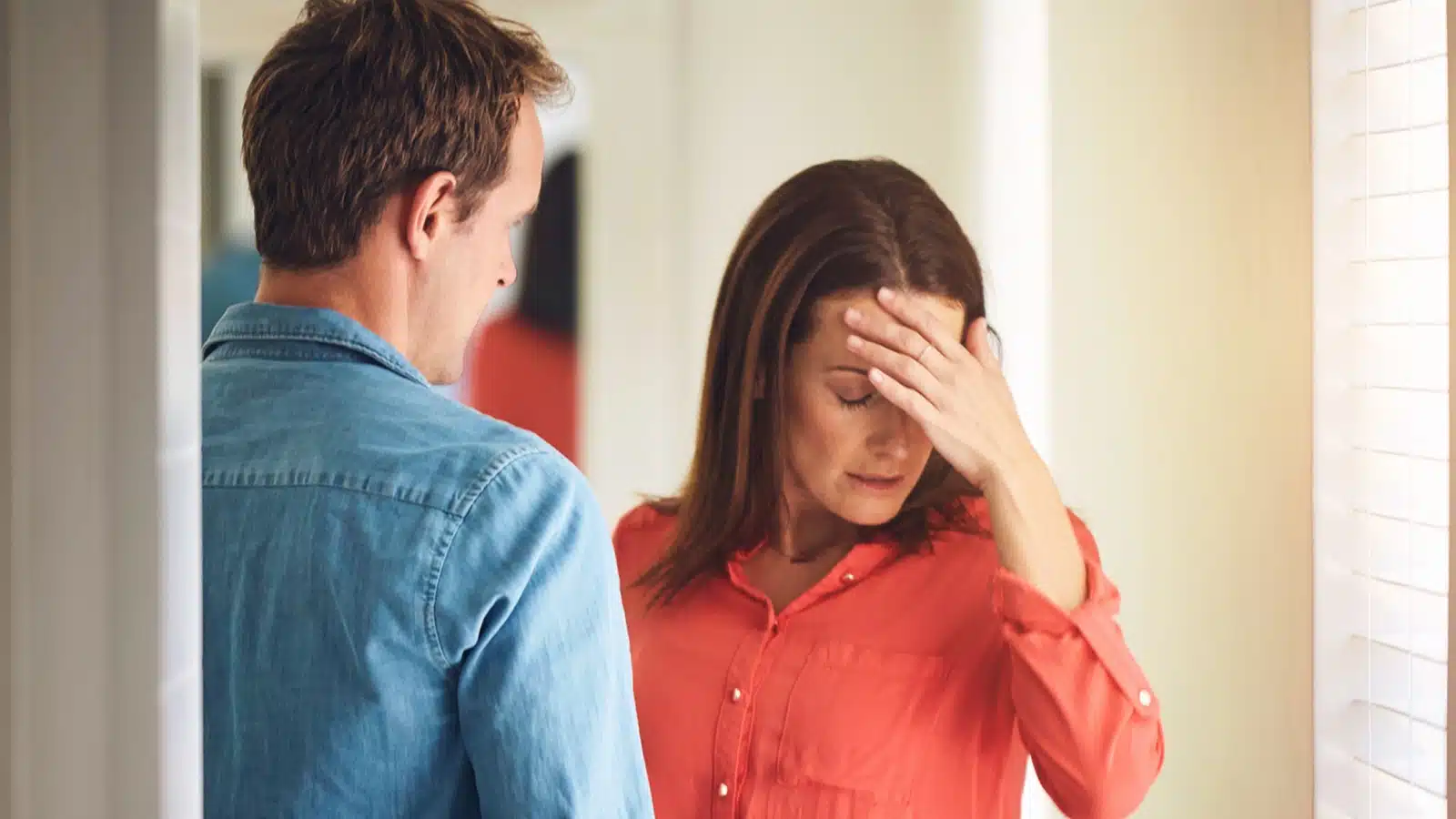 A stressed out woman has her hand on her head during a fight with her husband, as if she's given up.