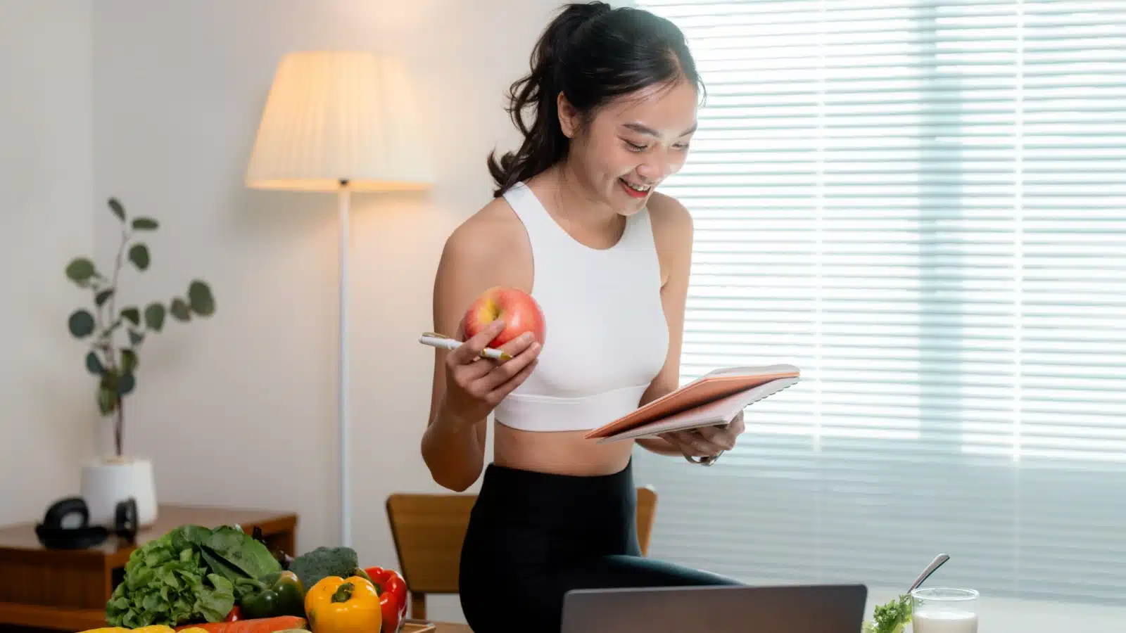 A woman holding an apple and a notebook, to highlight that she's tracking her calories.
