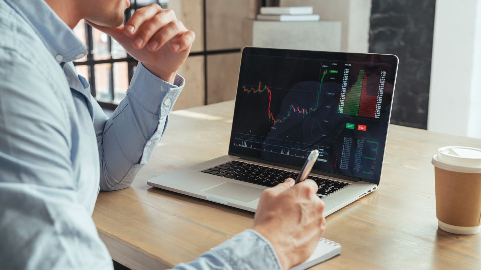 A man sits in front of a computer, tracking a stock as it rises, to represent unrealized gains.