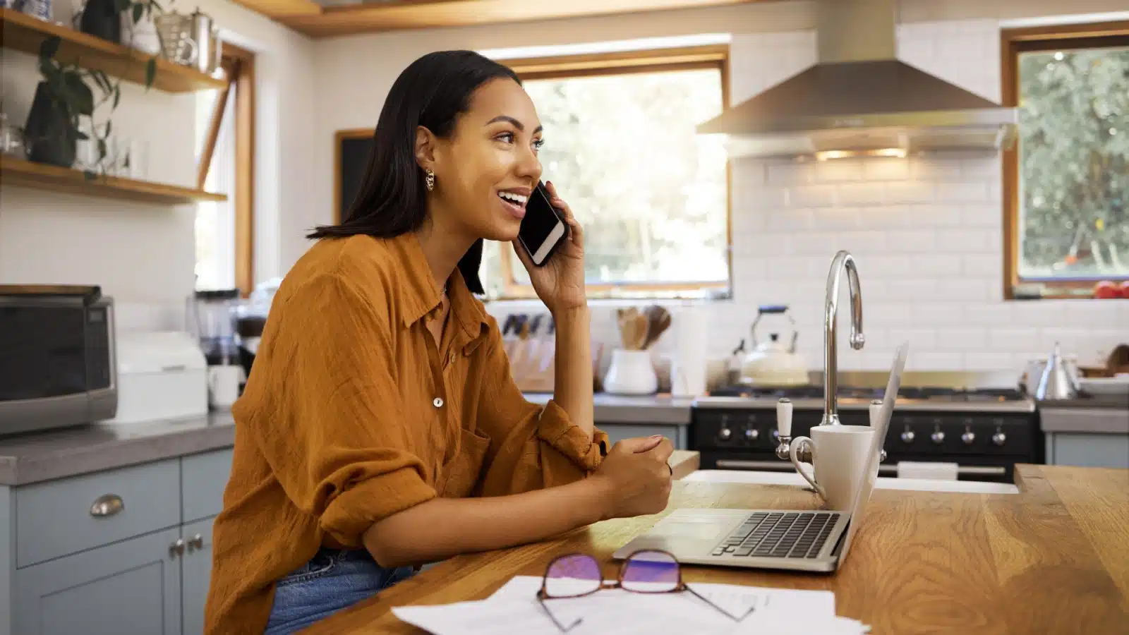 A smiling woman talks on the phone while working on her budget to represent cancelling a service.