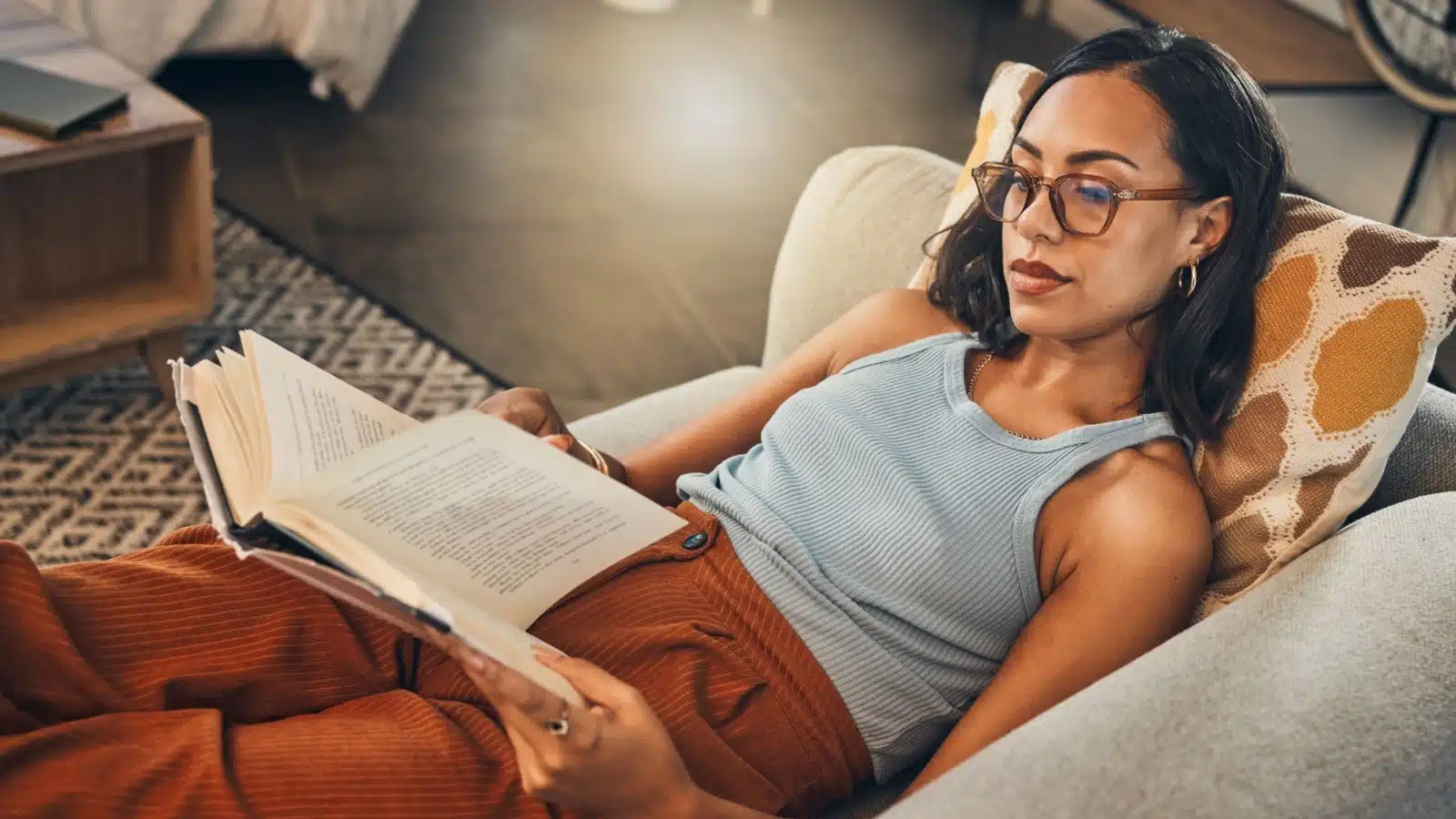 A woman relaxes on the couch, reading a novel.