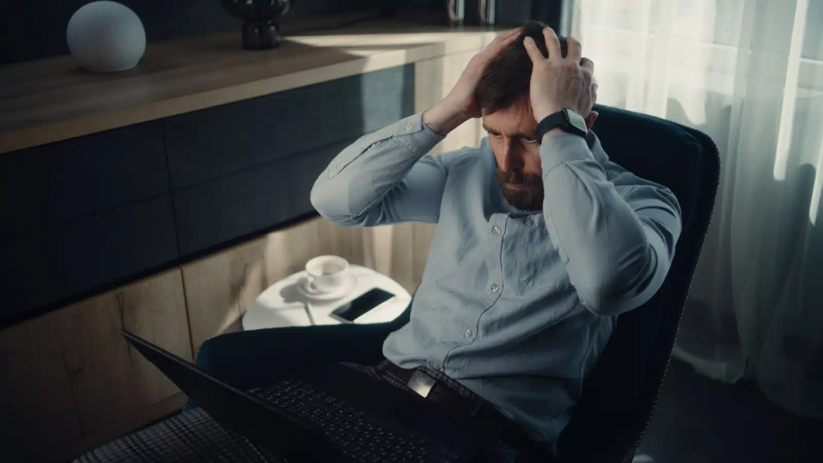 A man holds his hands to his head in shock, staring at his computer screen, because he lost all his money in a risky investment.
