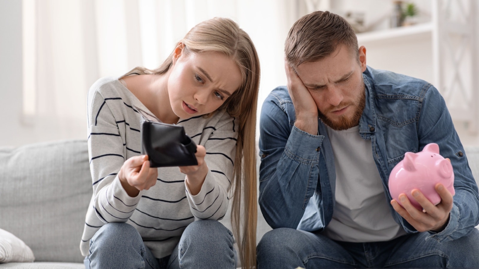 A young couple sits on the couch, stressed that they have no money.