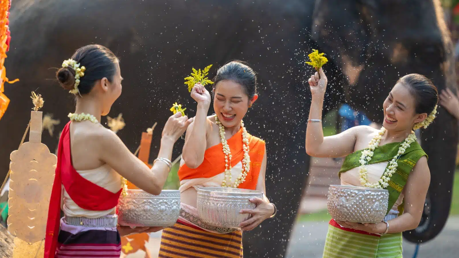 Thai women in traditional dress splash water on each other in celebration of the Songkran Festival.