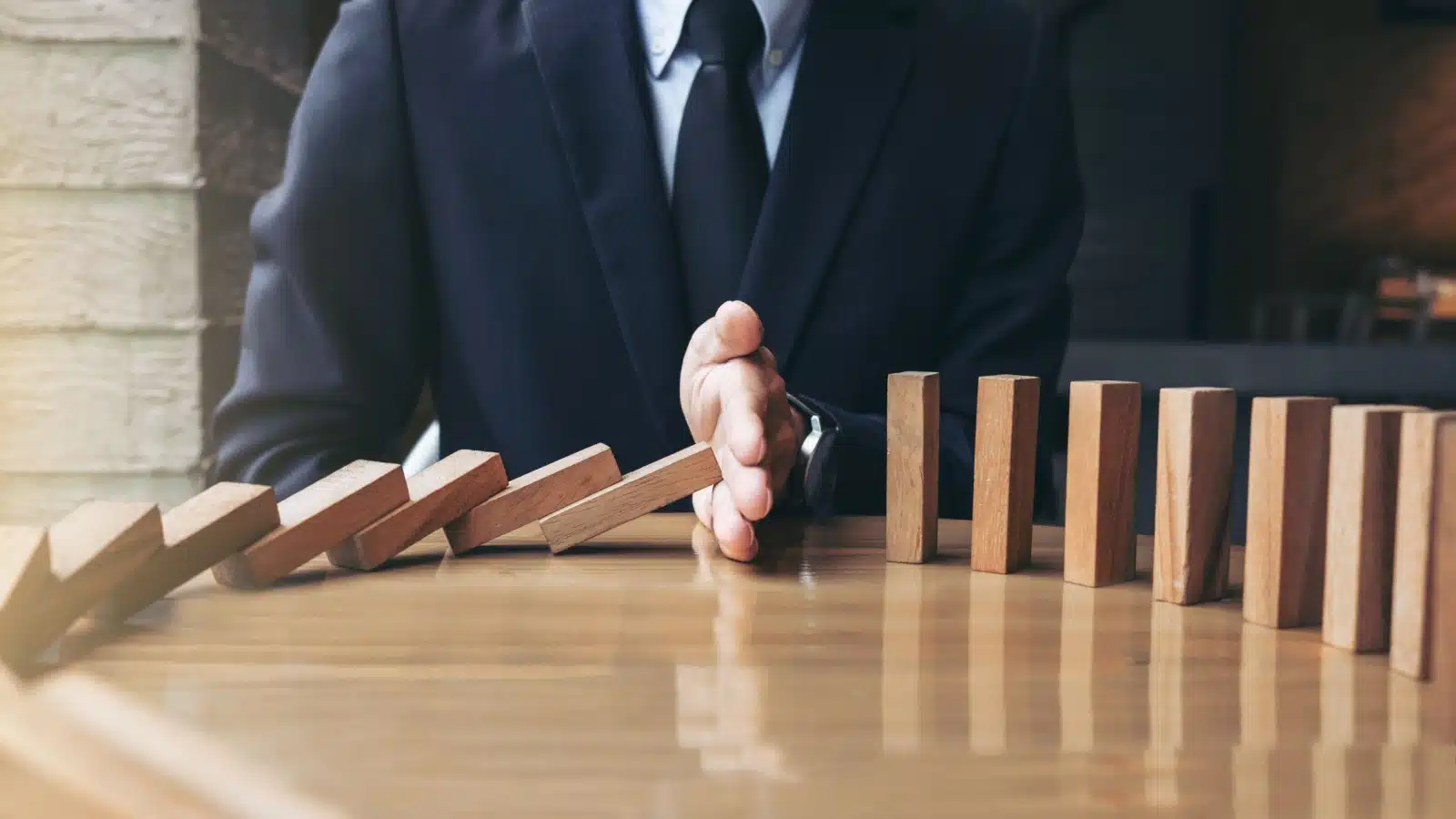 A businessman stops wooden dominos from falling to represent change management.