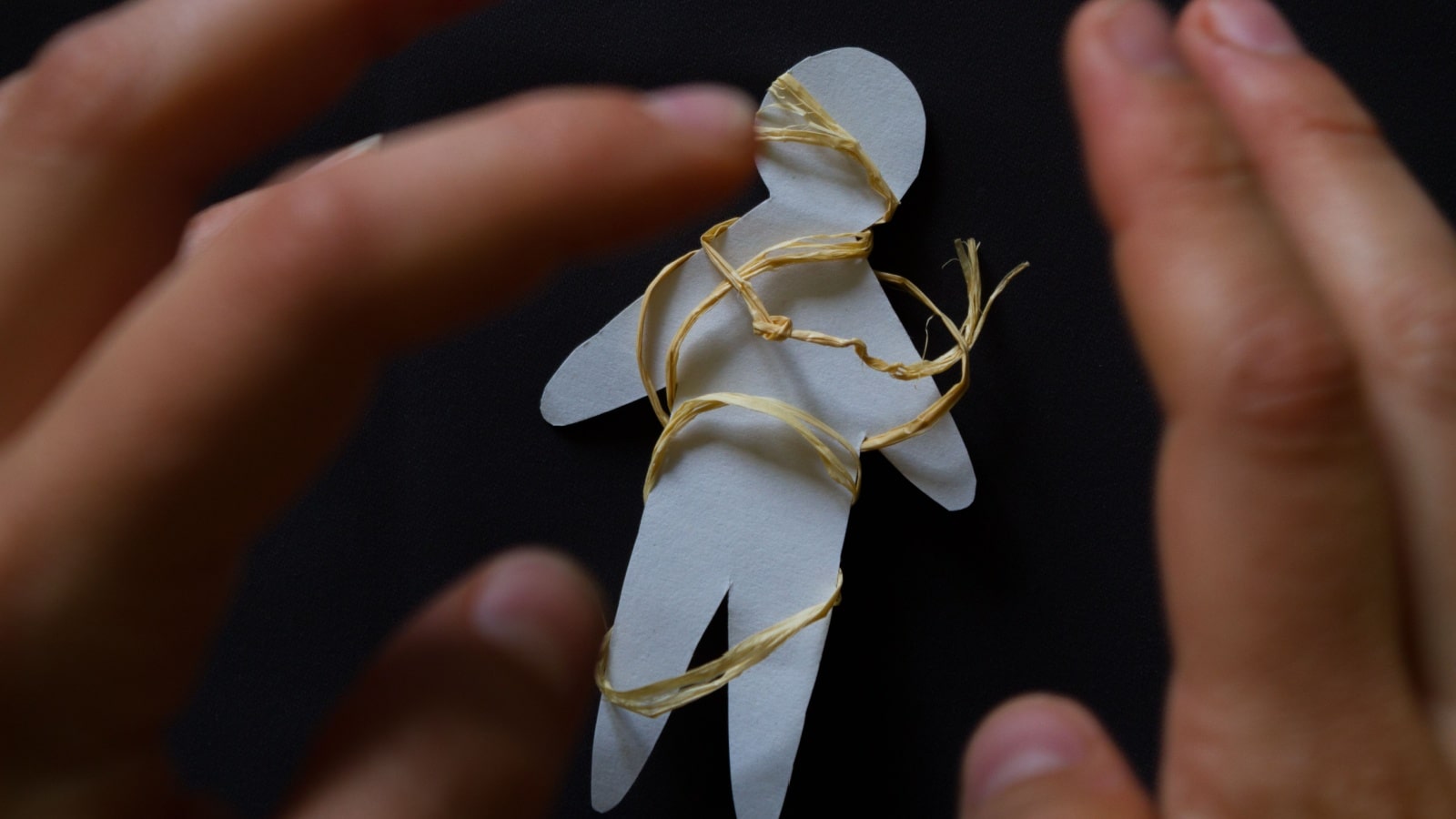 Hands wrapping a paper Voodoo figure to represent curses.