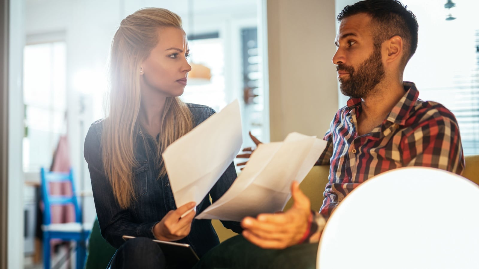 A couple sits on the couch, bills in hand, fighting about money.