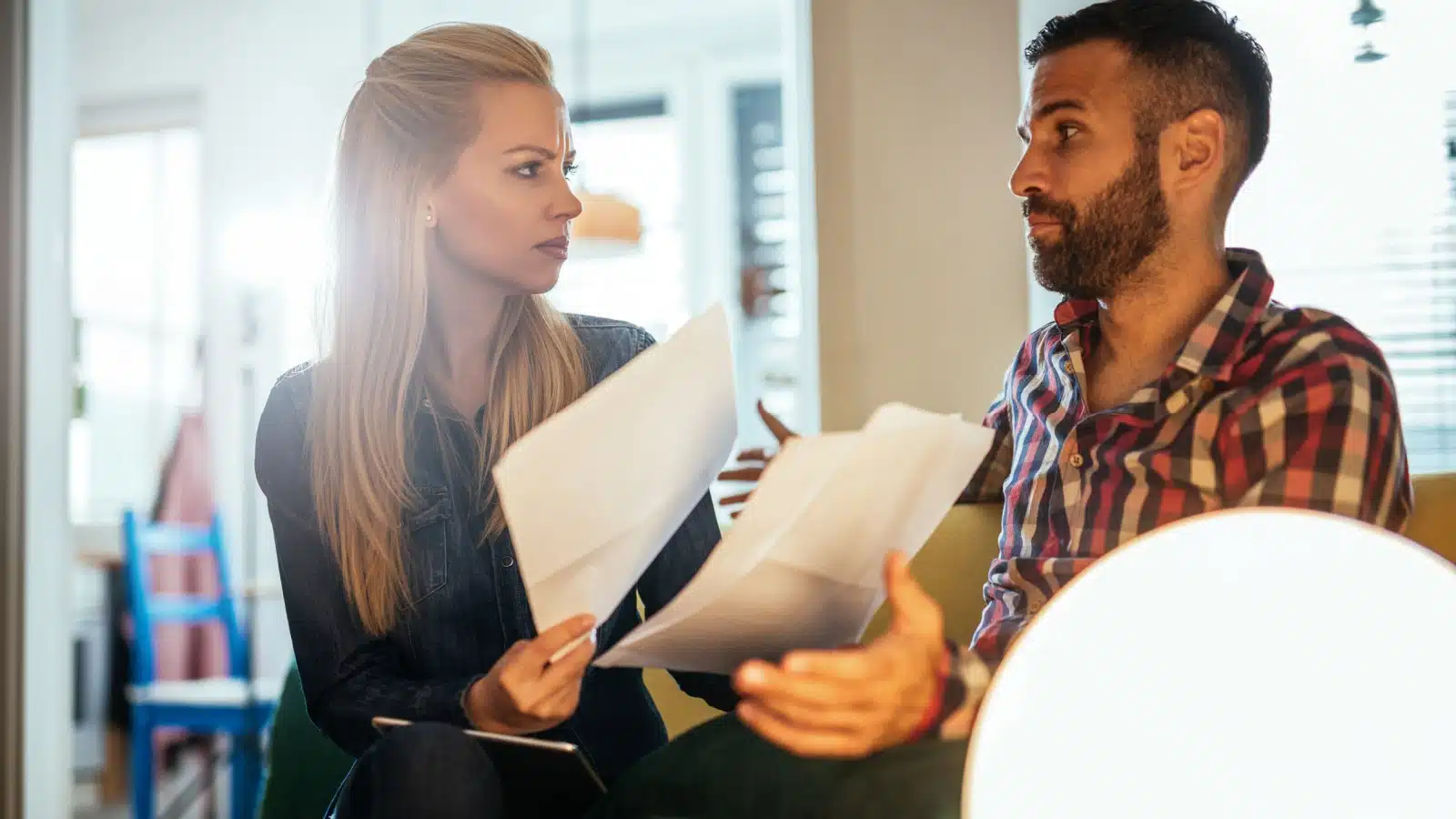 A couple sits on the couch, bills in hand, fighting about money.