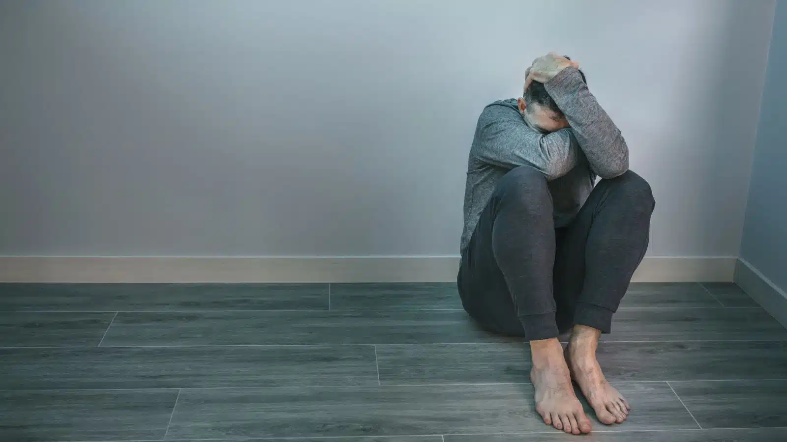 What does depression feel like? A man sits alone in a dark room, covering his head in sorrow to represent how depression feels.