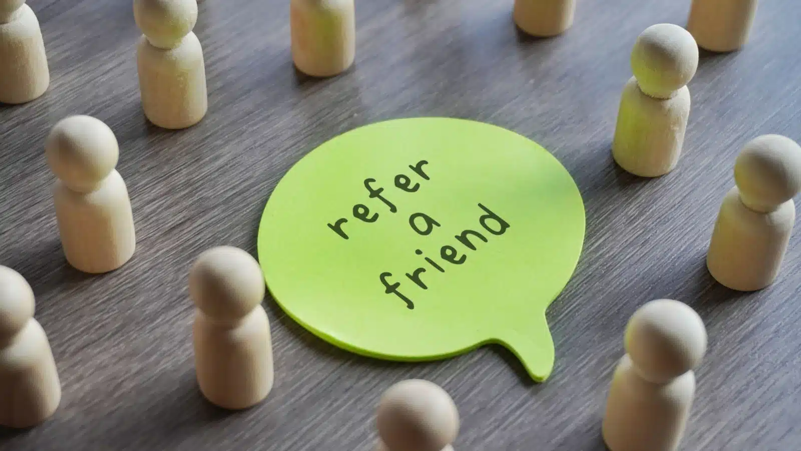 Little square pegs that represent people surrounding a sign that says "refer a friend."