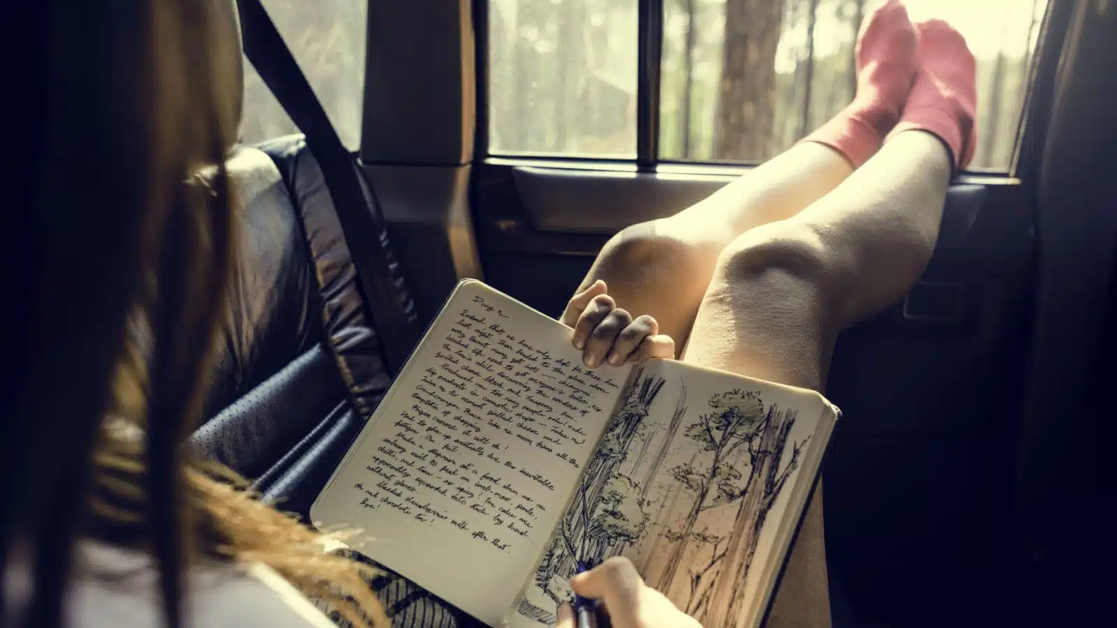 A woman journals in the backseat of a car during a road trip.