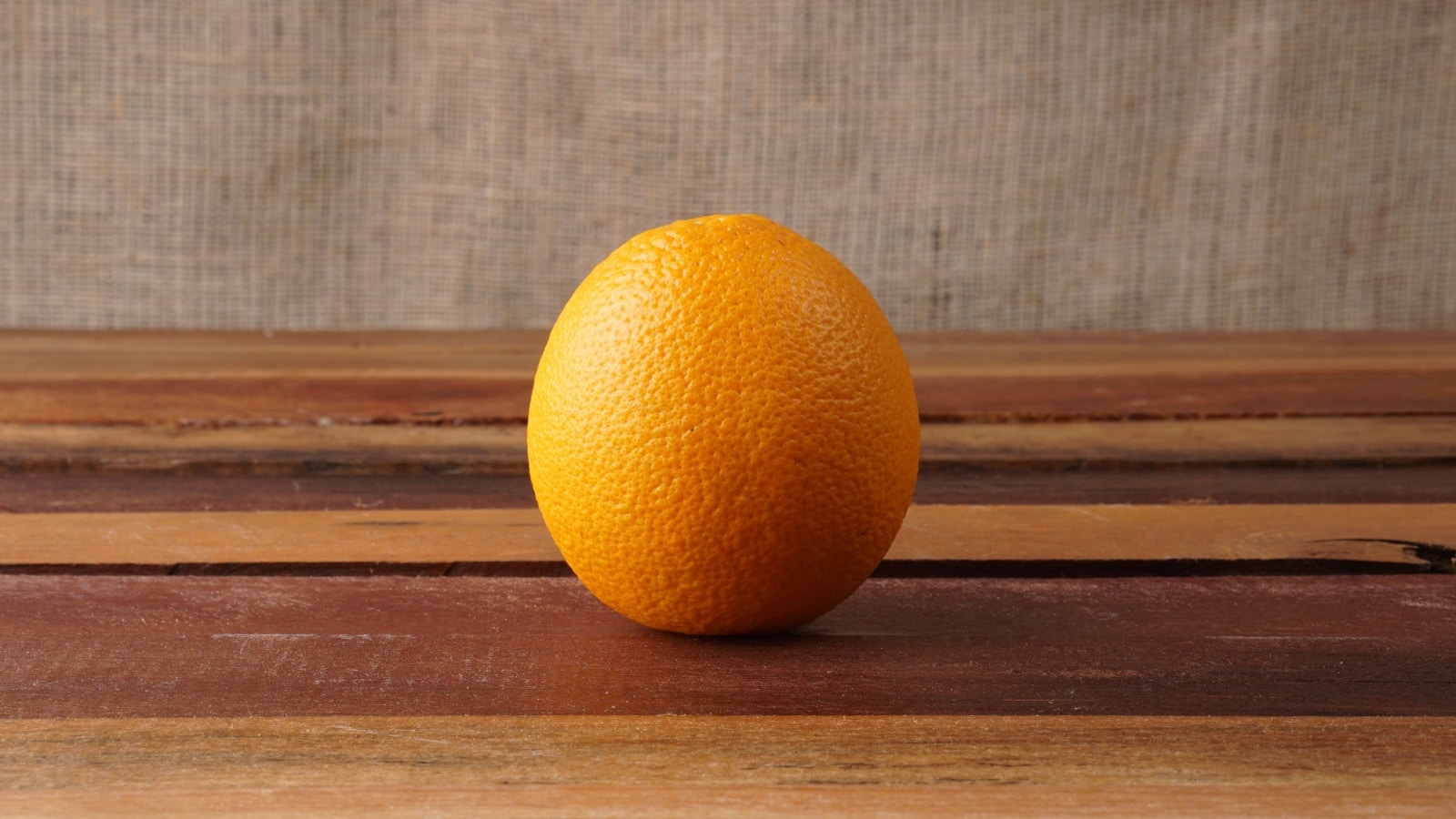 A single orange on a table. The light hits the orange from the left, casting a shadow to the right.