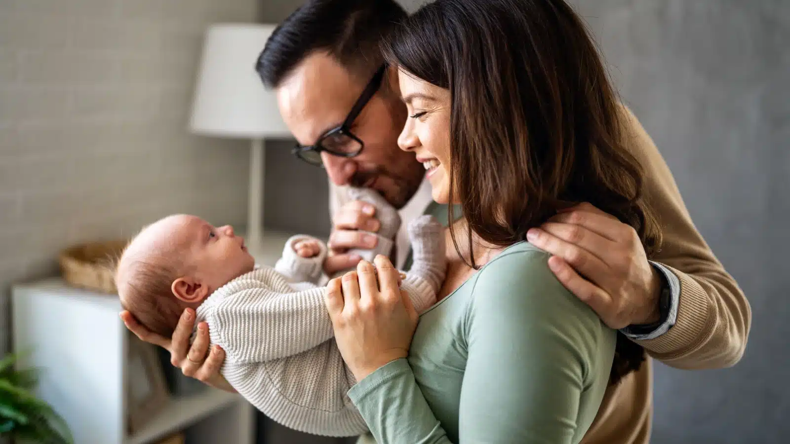 A happy couple snuggling their newborn baby to represent things to talk about before having a baby.