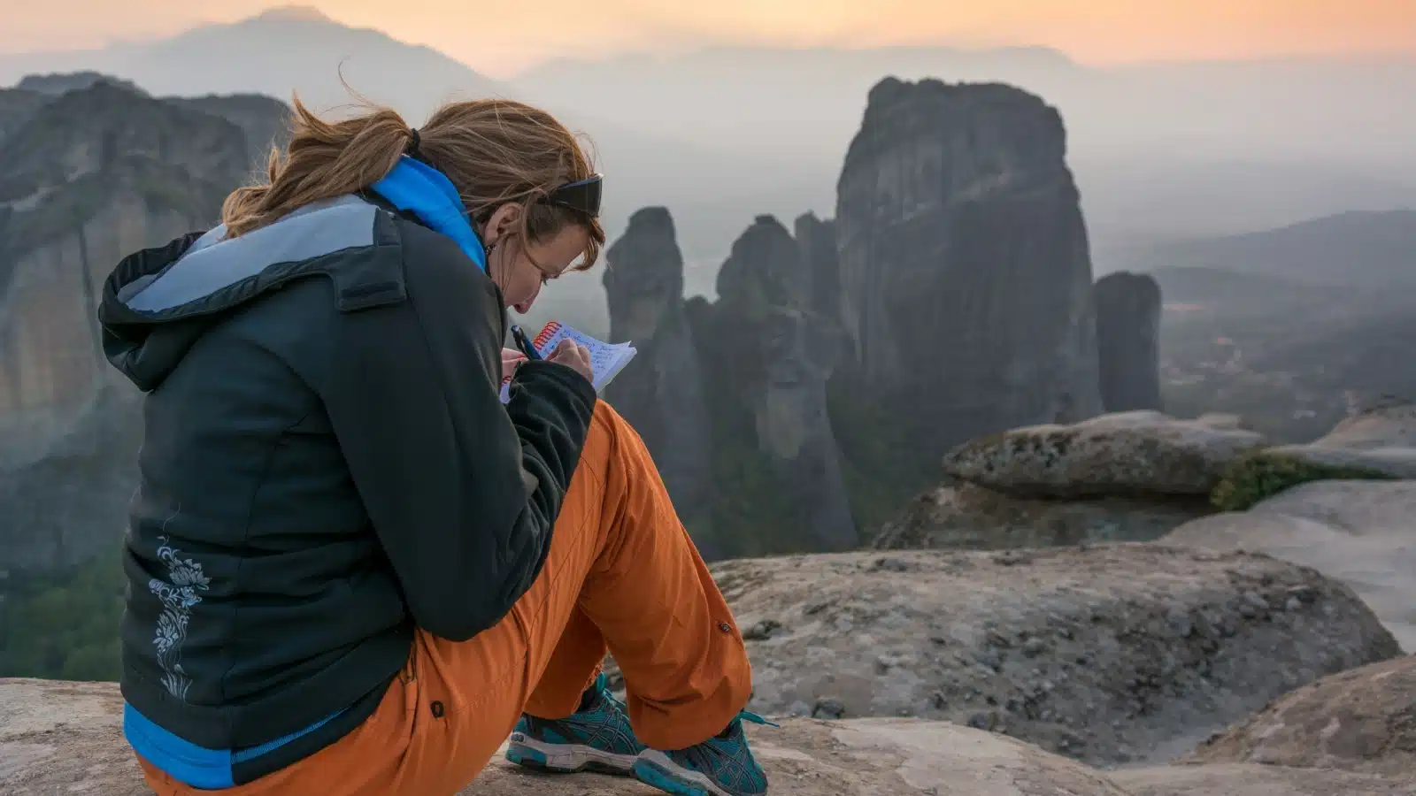 A hiker writes her thoughts in her journal after finding a spectacular view.