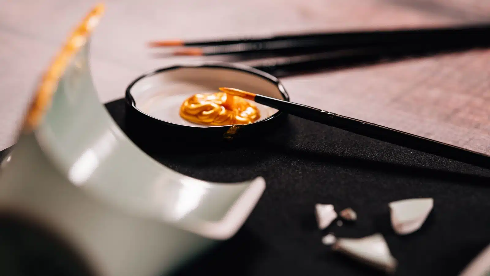 A close-up of a broken piece of pottery and gold paint, representing the question "what is kintsugi"