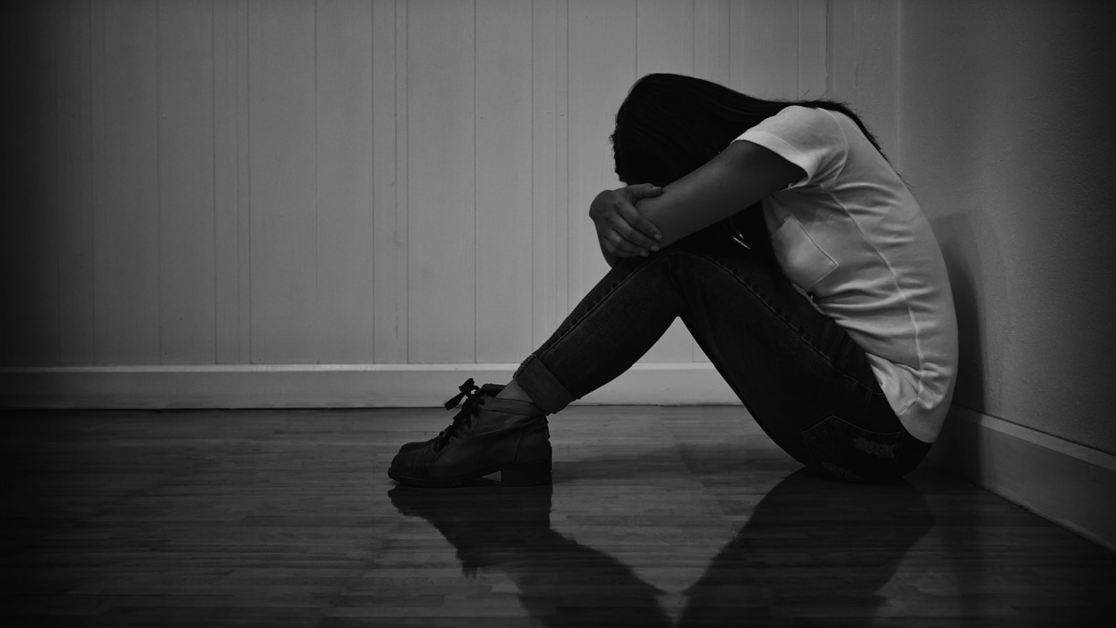 A black & white image of a woman crying in the corner, representing an abusive relationship and begging the question "why doesn't she leave."