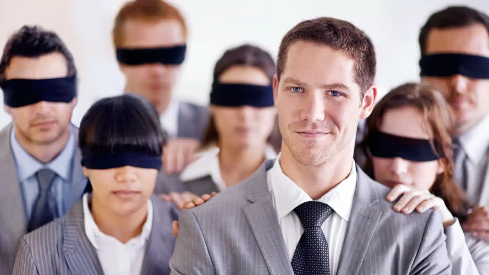 A group of blind-folded workers gather behind their leader, the only person without a blindfold, to highlight why leadership skills matter.