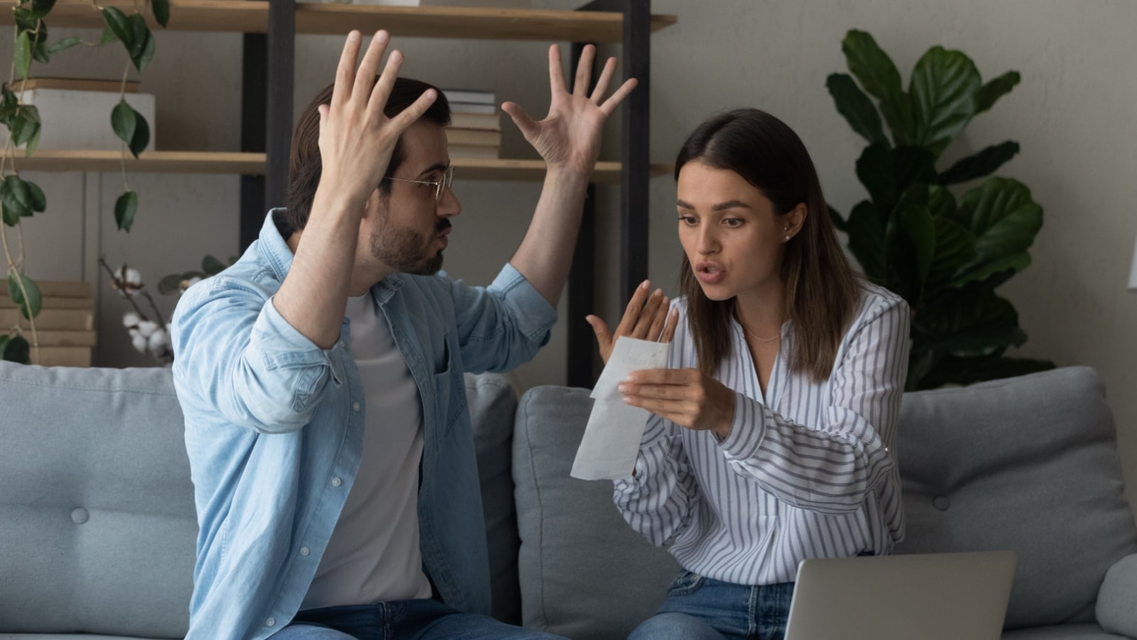 A couple sits on the couch, arguing over a receipt.