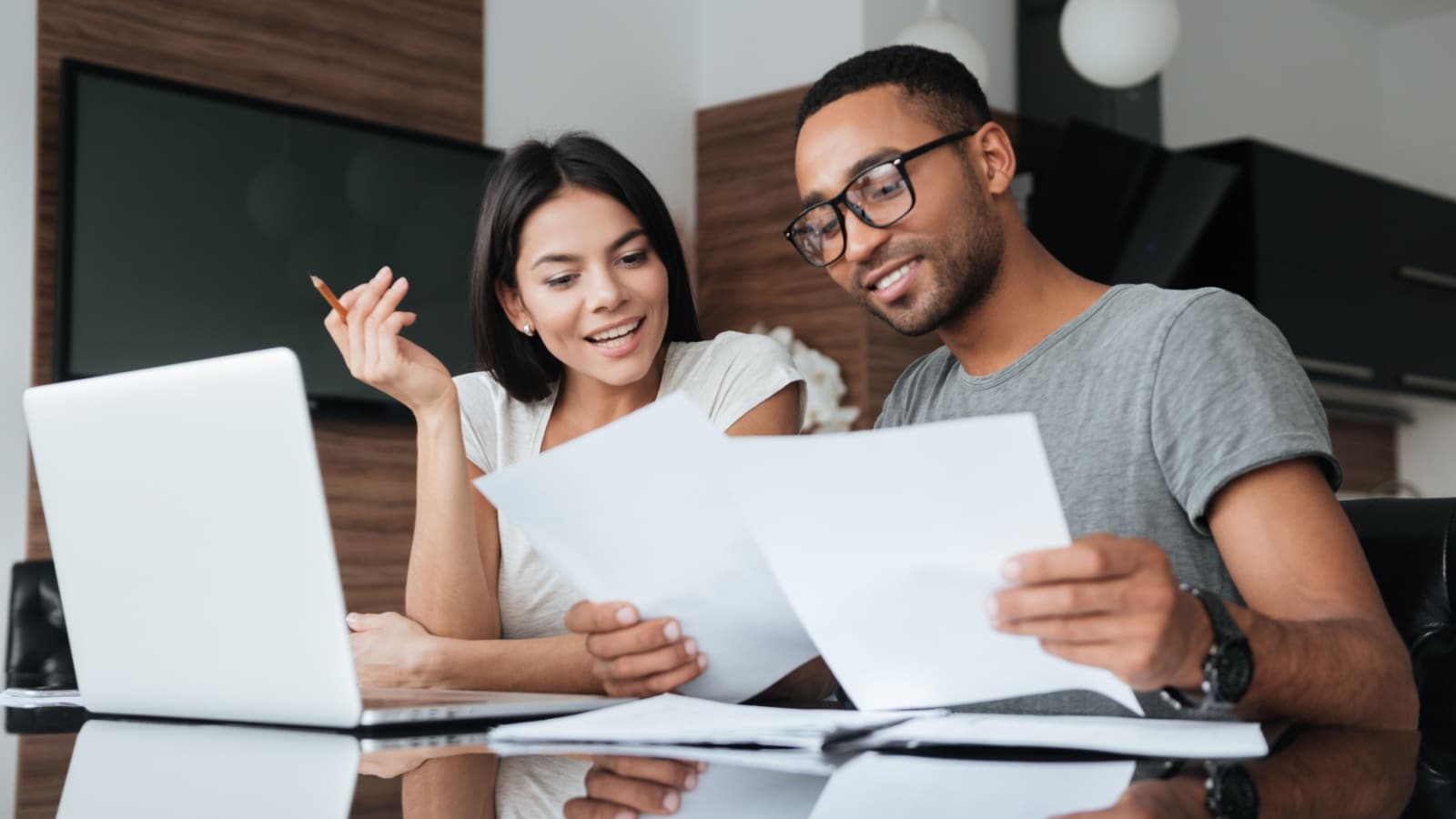 A happy couple sits at a laptop reviewing paperwork together.