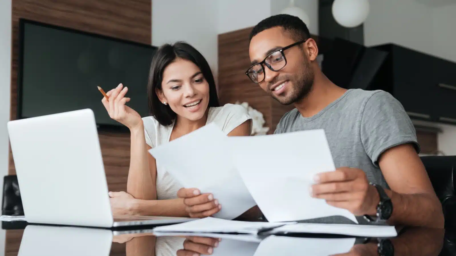 A happy couple sits at a laptop reviewing paperwork together.
