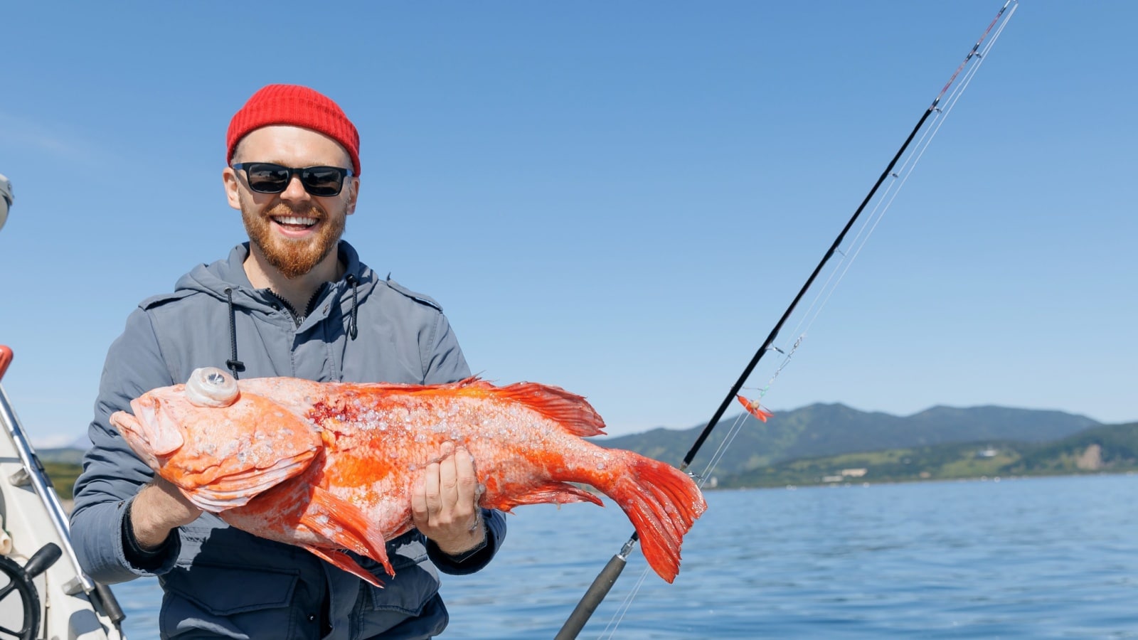 A man holds up a red perch he caught during a deep sea sports fishing expedition.