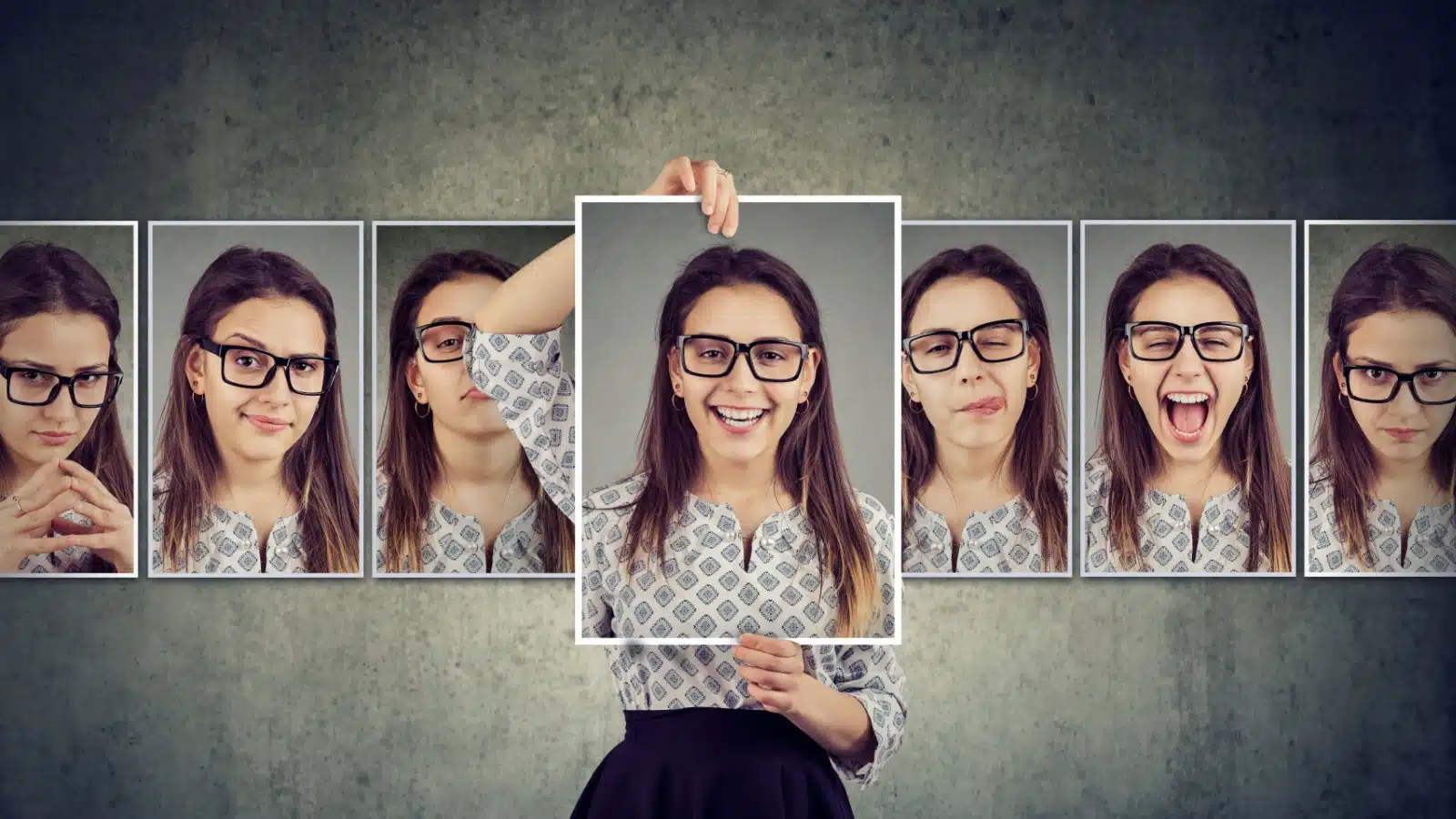 A girl holds portraits of herself showcasing a variety of facial expressions.