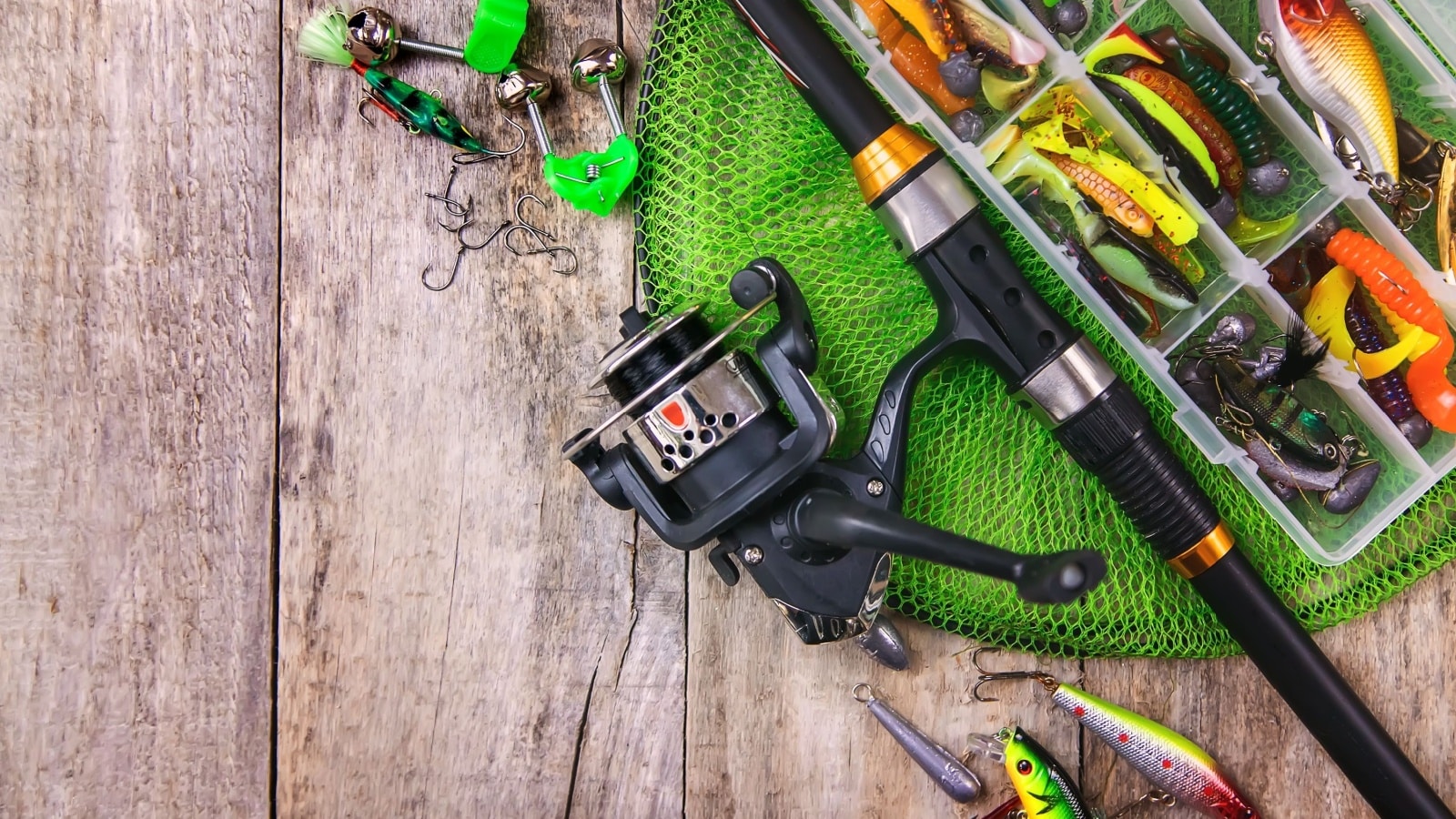 Fishing gear including a close up of a rod with reel, lures, and a net. 