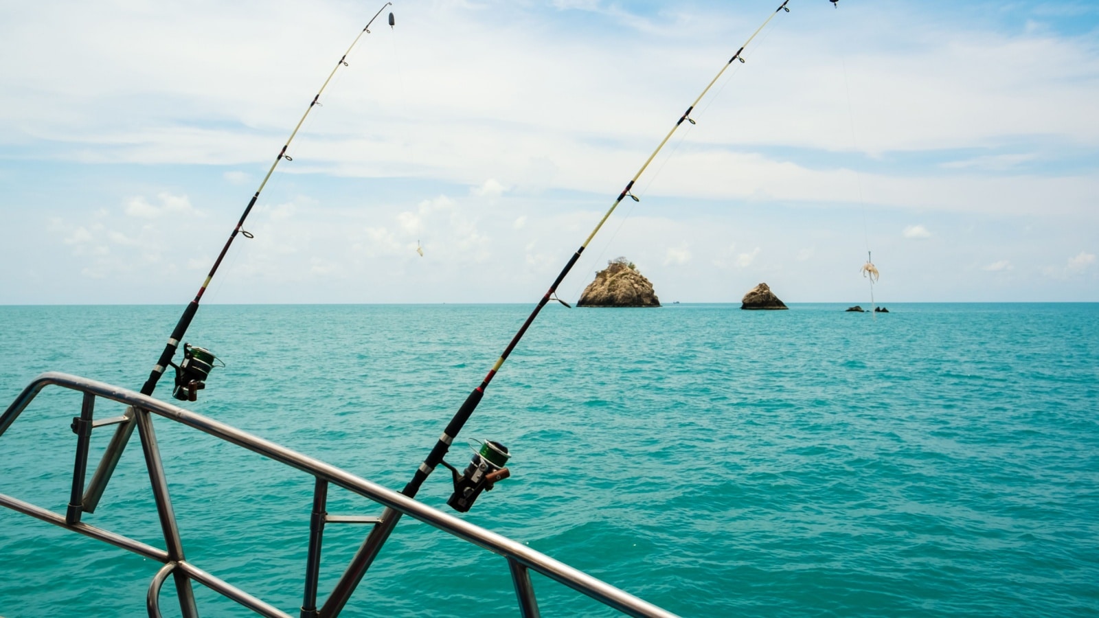 Two fishing poles attached to the railing of a deep sea fishing vessel. 