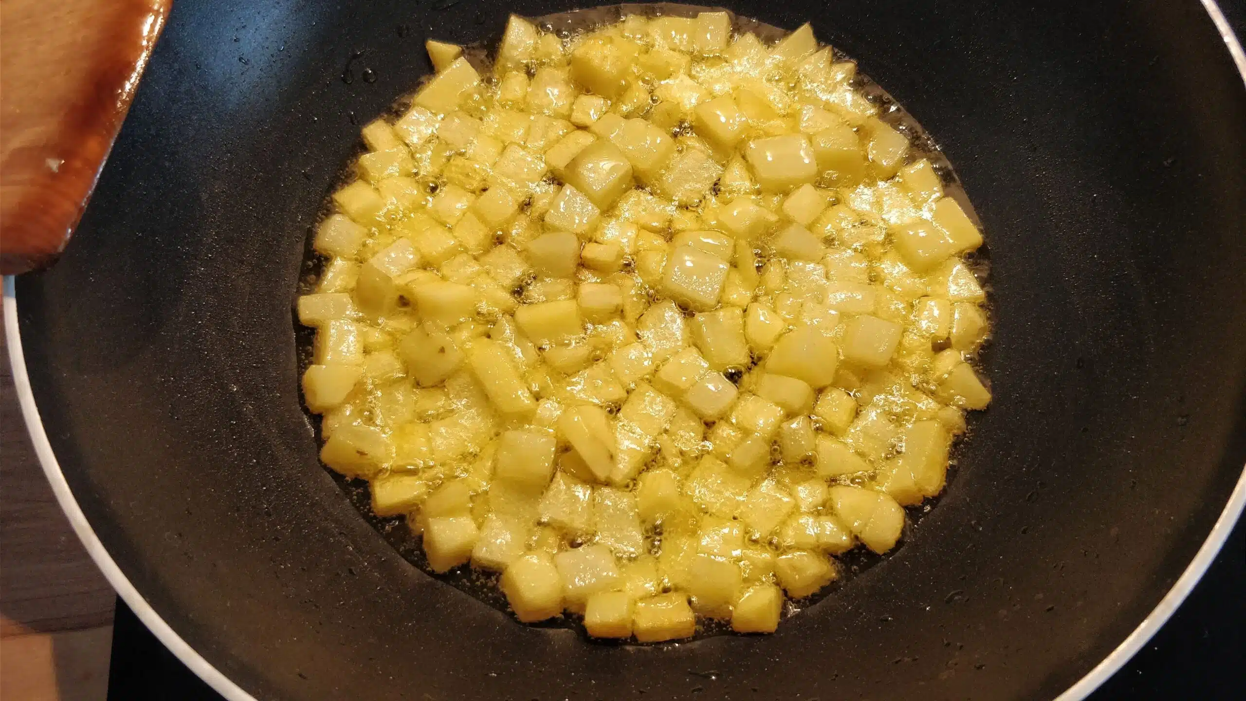 Potato cubes sizzling in a frying pan.